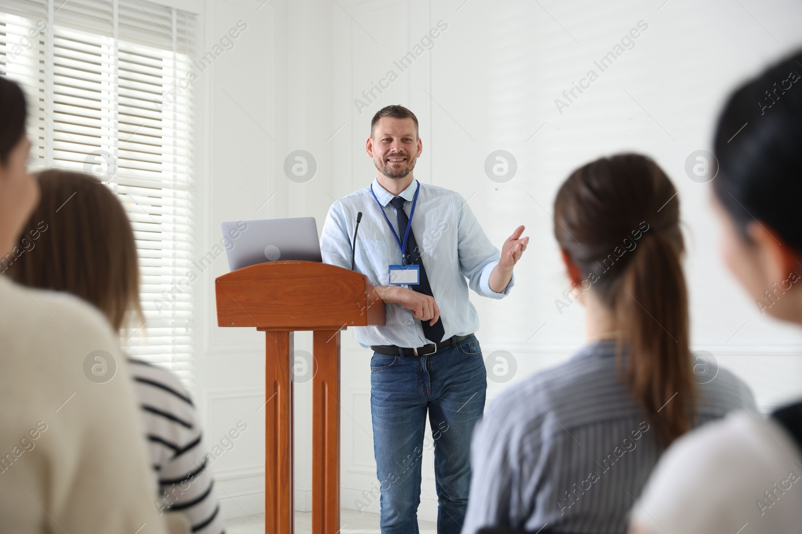 Photo of Man giving public speech at lectern in front of audience indoors