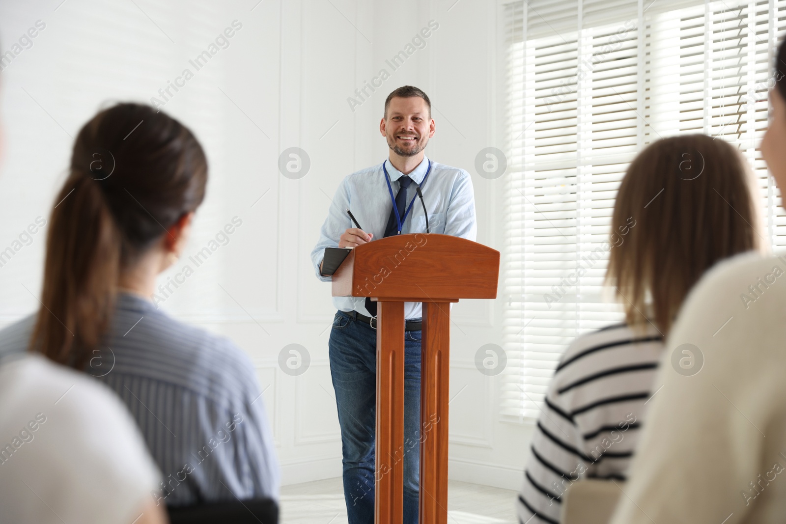 Photo of Man giving public speech at lectern in front of audience indoors