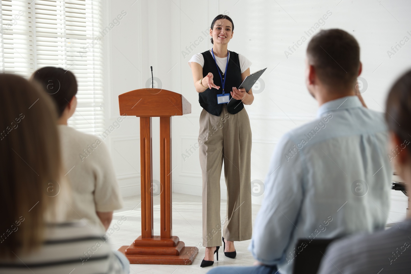Woman giving public speech at lectern in front of audience indoors Photo of Woman giving public speech at lectern in front of audience indoors