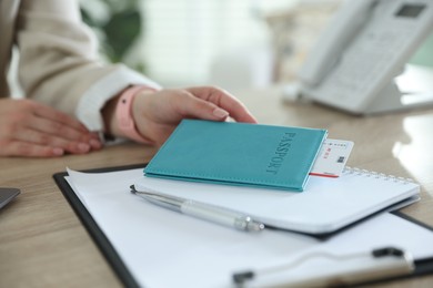 Photo of Travel agent with passport and ticket at wooden table in office, closeup