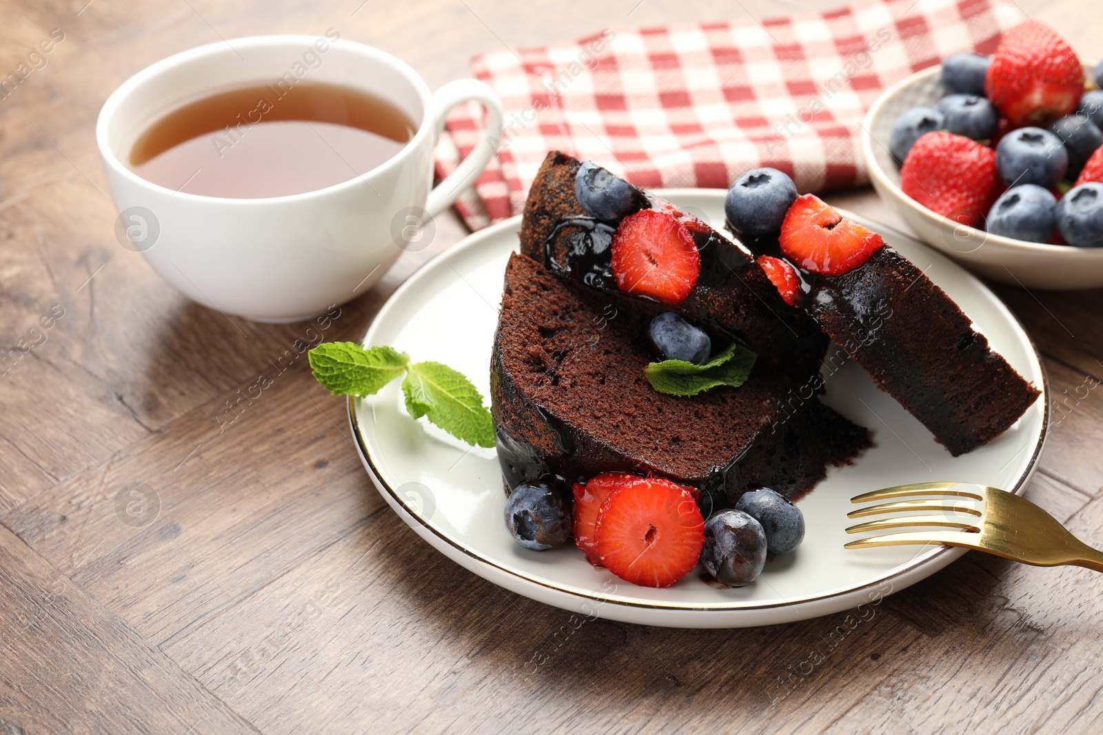 Pieces of delicious chocolate bundt cake with strawberries and blueberries on wooden table, closeup Photo of Pieces of delicious chocolate bundt cake with strawberries and blueberries on wooden table, closeup