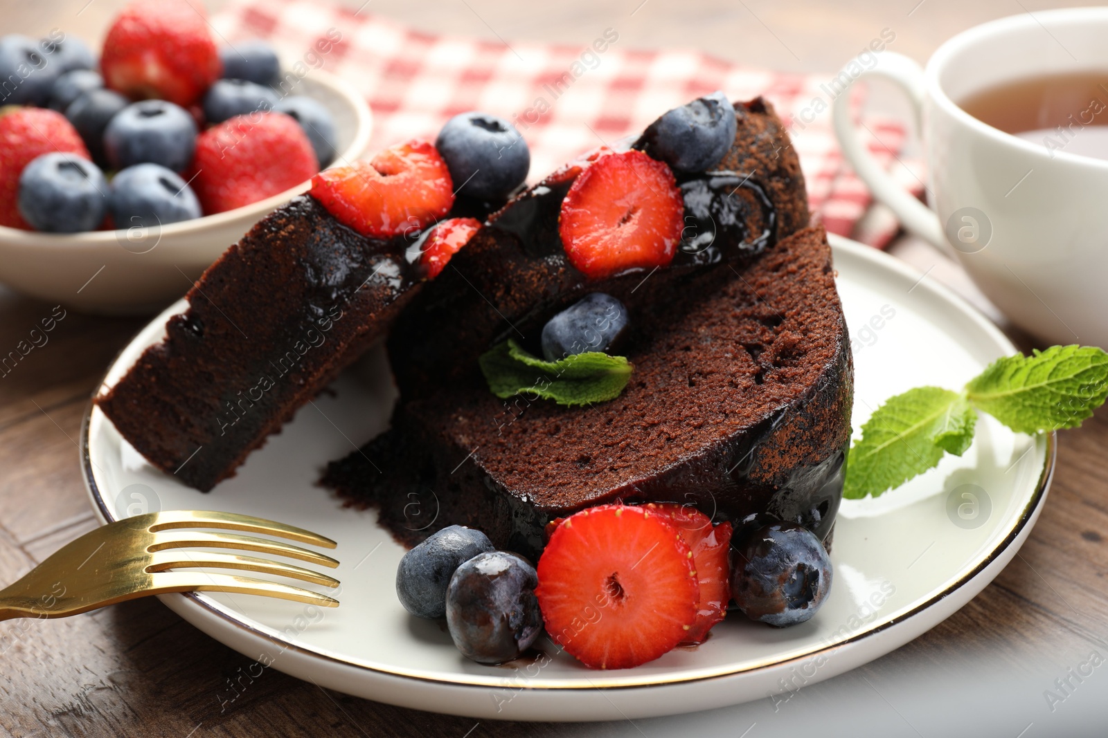 Pieces of delicious chocolate bundt cake with strawberries and blueberries on wooden table, closeup Photo of Pieces of delicious chocolate bundt cake with strawberries and blueberries on wooden table, closeup