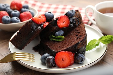Photo of Pieces of delicious chocolate bundt cake with strawberries and blueberries on wooden table, closeup