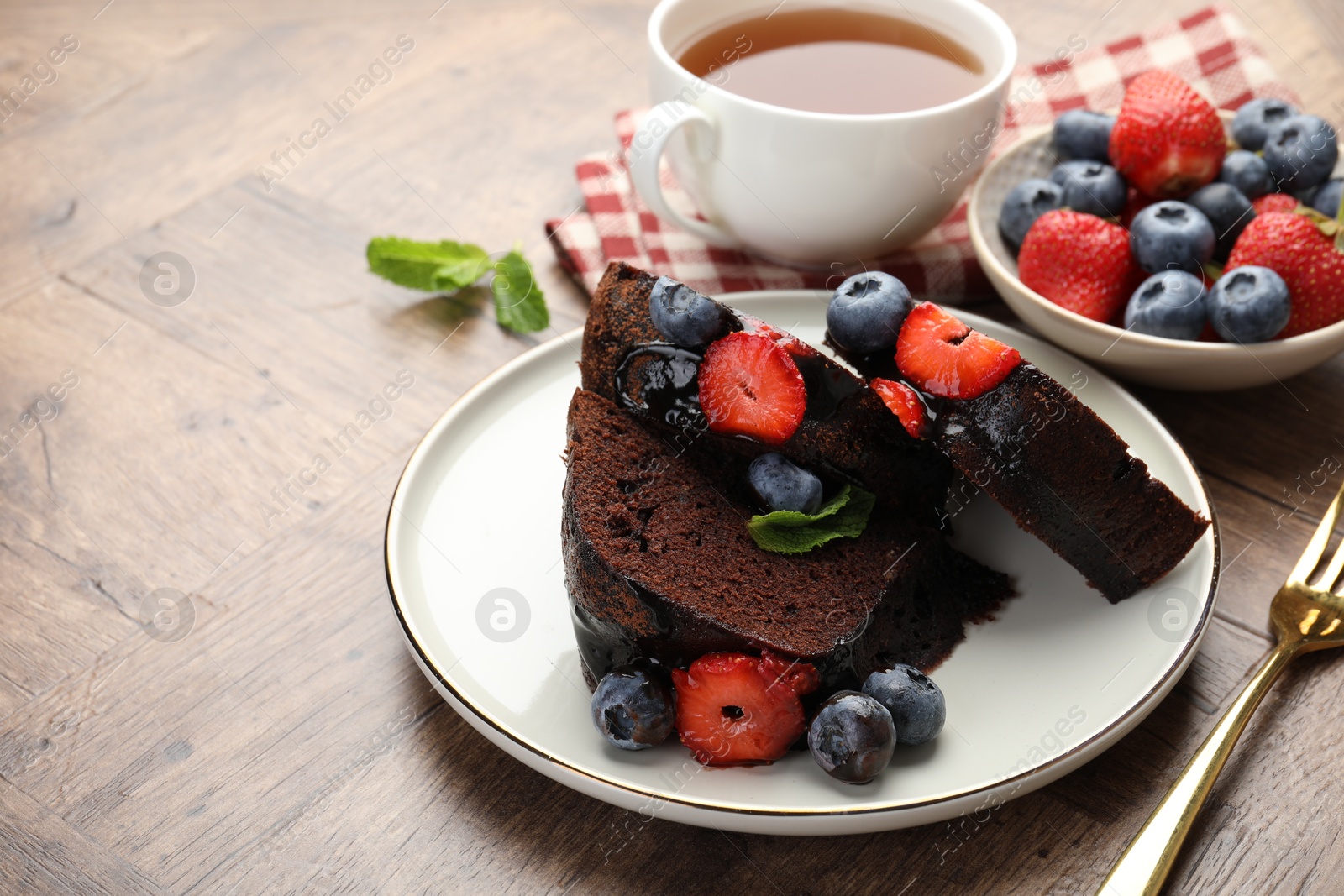 Pieces of delicious chocolate bundt cake with strawberries and blueberries on wooden table, closeup Photo of Pieces of delicious chocolate bundt cake with strawberries and blueberries on wooden table, closeup