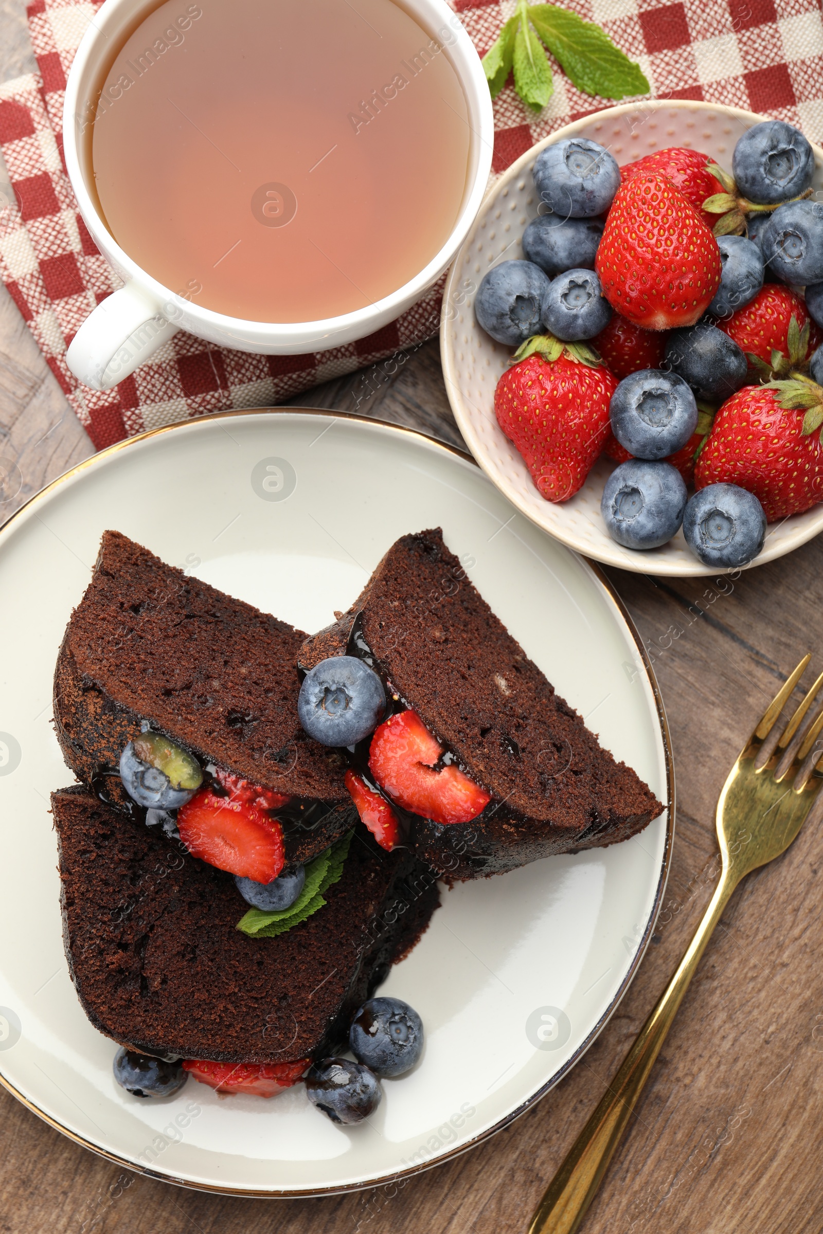 Pieces of delicious chocolate bundt cake with strawberries and blueberries served on wooden table, flat lay Photo of Pieces of delicious chocolate bundt cake with strawberries and blueberries served on wooden table, flat lay