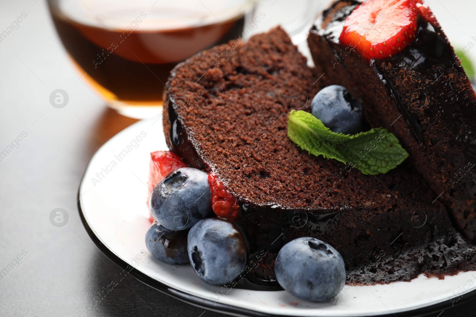 Pieces of delicious chocolate bundt cake with strawberries, mint and blueberries on grey table, closeup Photo of Pieces of delicious chocolate bundt cake with strawberries, mint and blueberries on grey table, closeup
