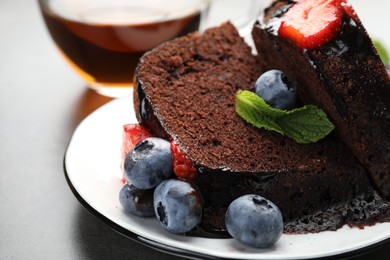 Photo of Pieces of delicious chocolate bundt cake with strawberries, mint and blueberries on grey table, closeup