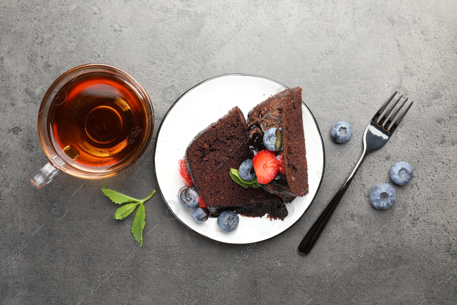 Pieces of delicious chocolate bundt cake with strawberries, mint and blueberries served on grey textured table, flat lay Photo of Pieces of delicious chocolate bundt cake with strawberries, mint and blueberries served on grey textured table, flat lay