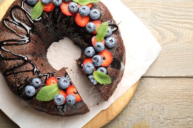 Photo of Delicious chocolate bundt cake with strawberries, mint and blueberries on wooden table, top view