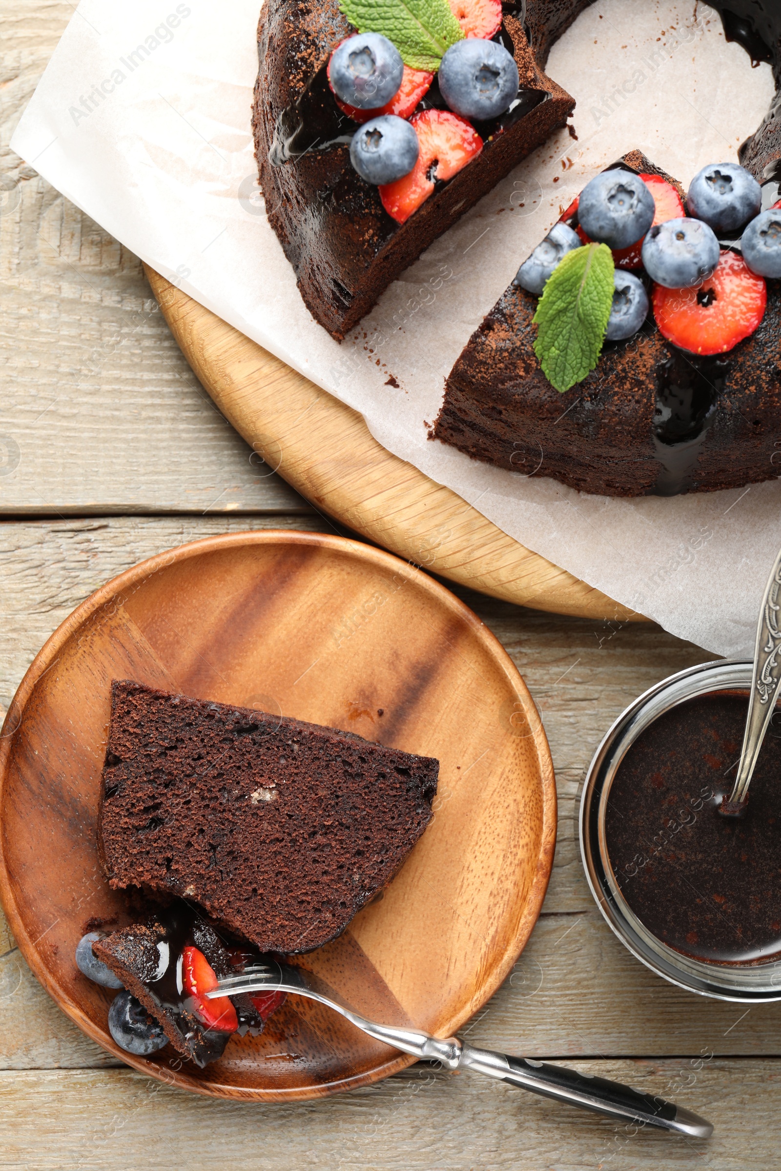 Delicious chocolate bundt cake with strawberries, mint and blueberries served on wooden table, flat lay Photo of Delicious chocolate bundt cake with strawberries, mint and blueberries served on wooden table, flat lay