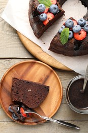 Photo of Delicious chocolate bundt cake with strawberries, mint and blueberries served on wooden table, flat lay