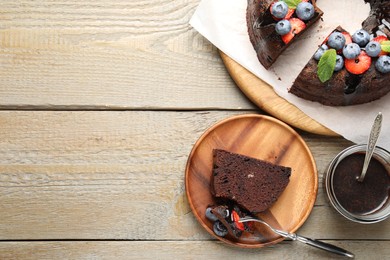 Photo of Delicious chocolate bundt cake with strawberries, mint and blueberries served on wooden table, flat lay. Space for text