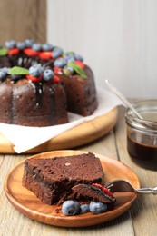 Photo of Delicious chocolate bundt cake with blueberries on wooden table, closeup