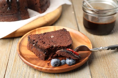 Photo of Piece of delicious chocolate bundt cake with blueberries on wooden table, closeup