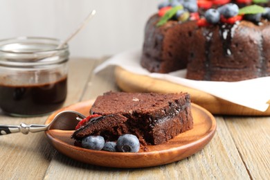 Photo of Piece of delicious chocolate bundt cake with blueberries on wooden table, closeup