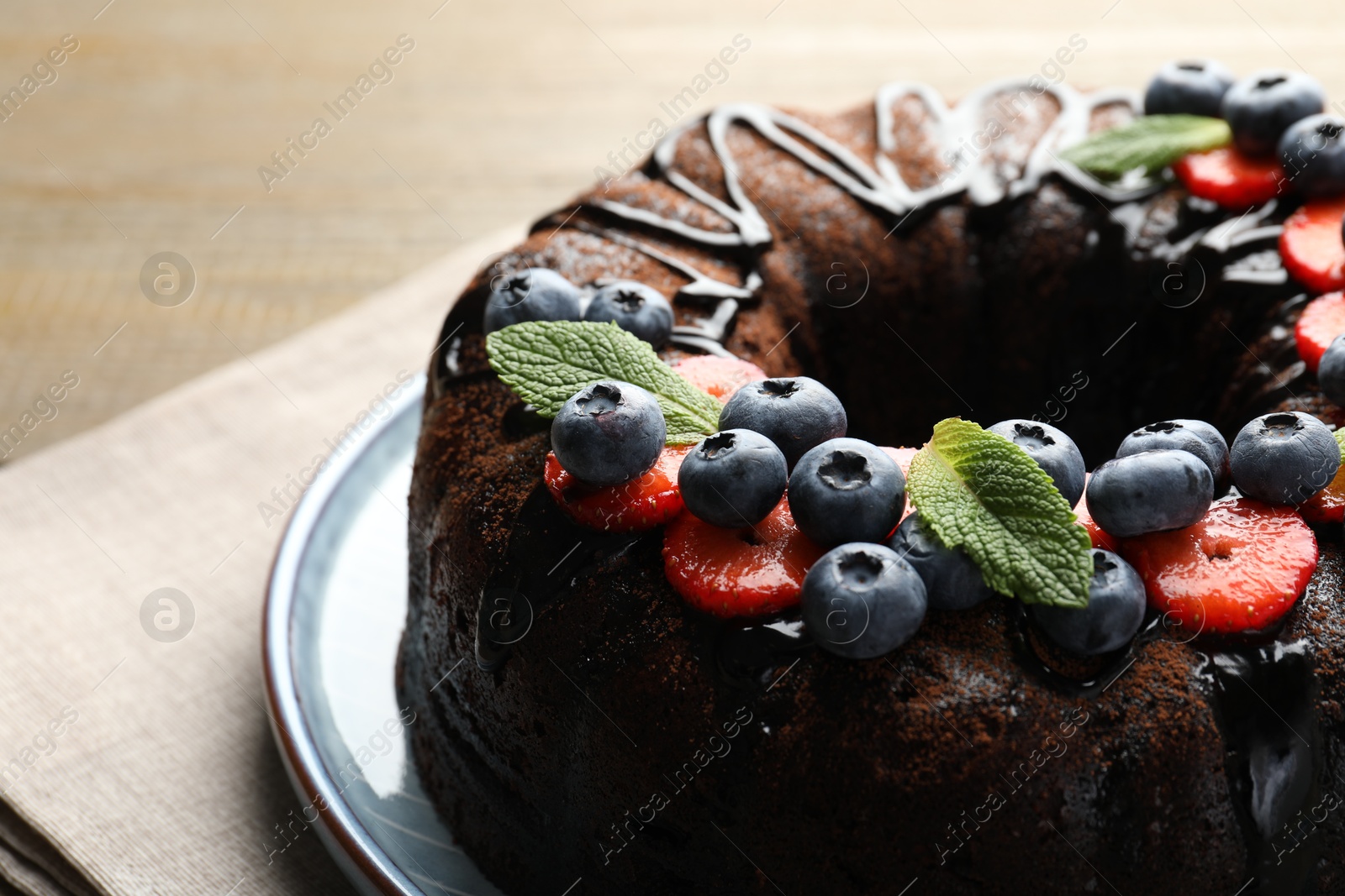 Delicious chocolate bundt cake with strawberries, mint and blueberries on table, closeup Photo of Delicious chocolate bundt cake with strawberries, mint and blueberries on table, closeup