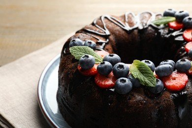 Photo of Delicious chocolate bundt cake with strawberries, mint and blueberries on table, closeup