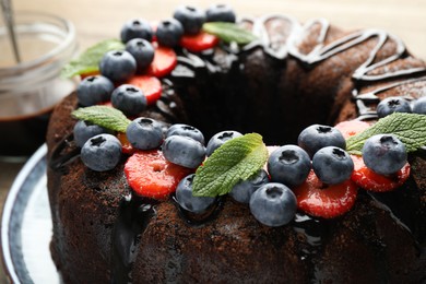 Photo of Delicious chocolate bundt cake with strawberries, mint and blueberries on table, closeup