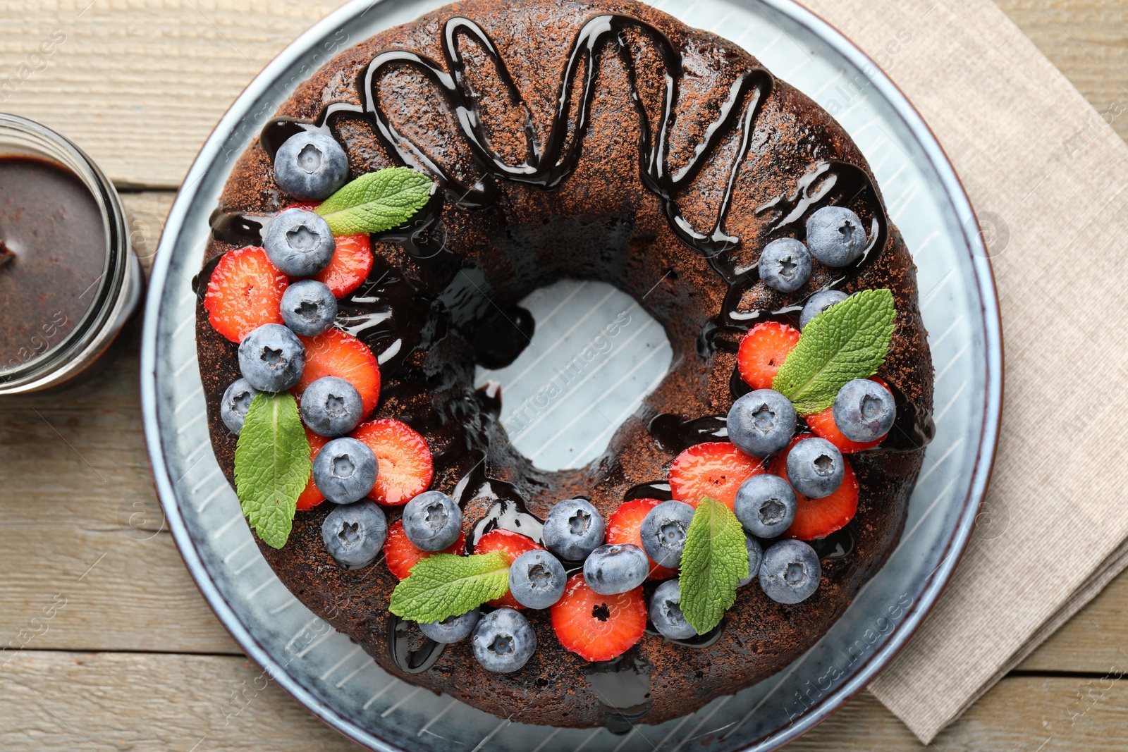 Delicious chocolate bundt cake with strawberries, mint and blueberries on wooden table, flat lay Photo of Delicious chocolate bundt cake with strawberries, mint and blueberries on wooden table, flat lay