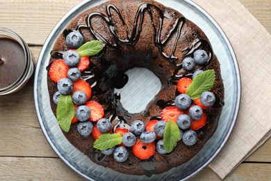 Photo of Delicious chocolate bundt cake with strawberries, mint and blueberries on wooden table, flat lay