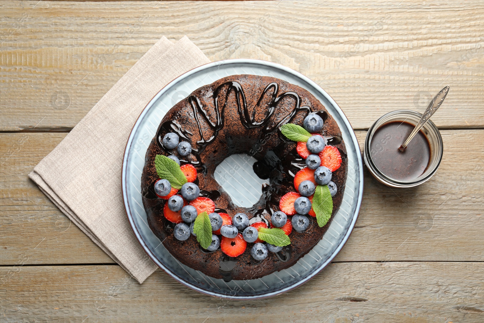 Delicious chocolate bundt cake with strawberries, mint and blueberries on wooden table, flat lay Photo of Delicious chocolate bundt cake with strawberries, mint and blueberries on wooden table, flat lay