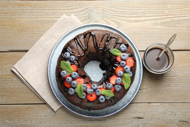 Photo of Delicious chocolate bundt cake with strawberries, mint and blueberries on wooden table, flat lay