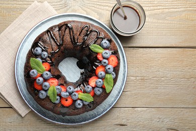 Photo of Delicious chocolate bundt cake with strawberries, mint and blueberries on wooden table, flat lay. Space for text