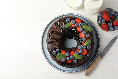 Photo of Delicious chocolate bundt cake with strawberries, mint and blueberries on light wooden table, flat lay. Space for text