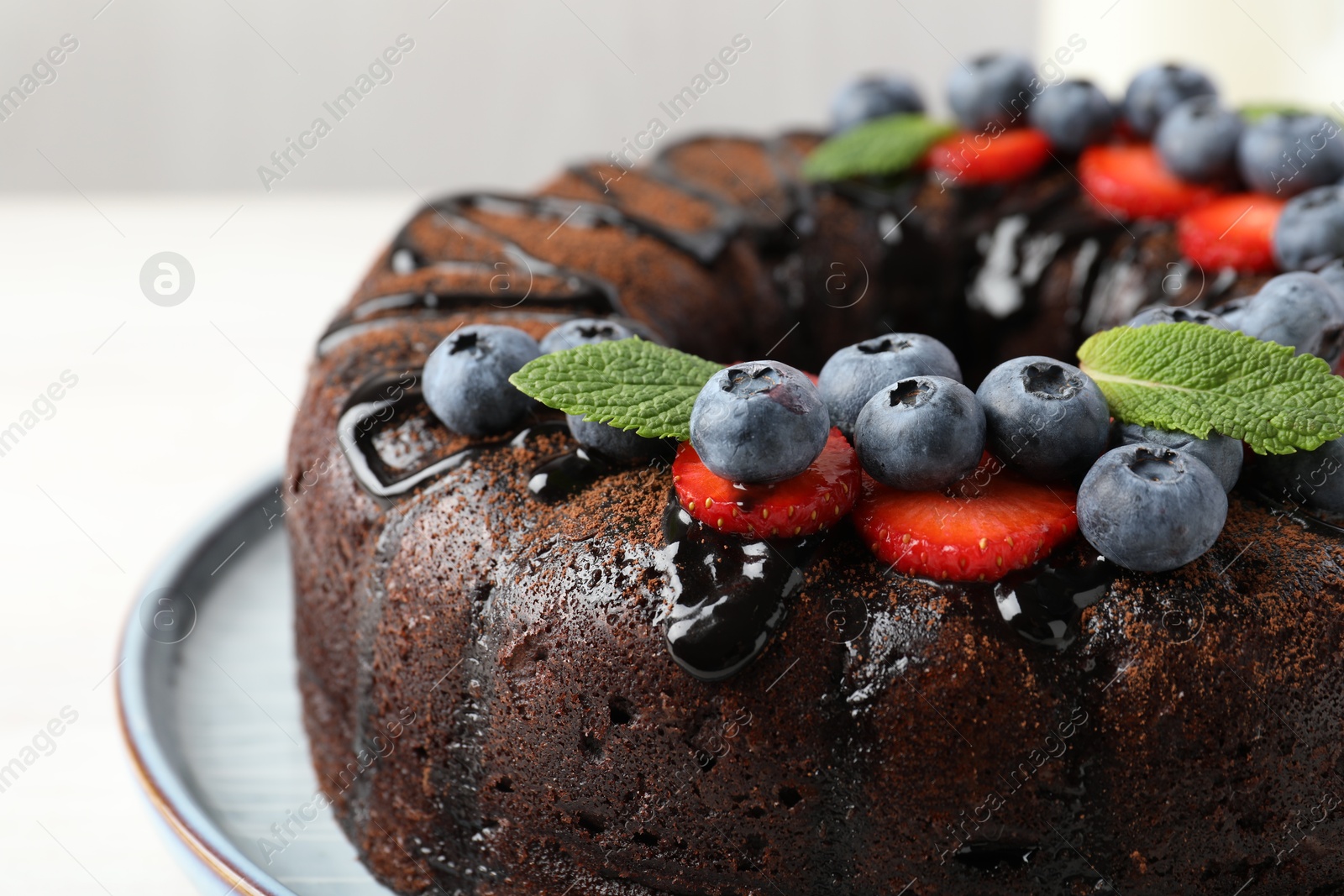Delicious chocolate bundt cake with strawberries, mint and blueberries on light table, closeup Photo of Delicious chocolate bundt cake with strawberries, mint and blueberries on light table, closeup