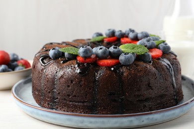 Photo of Delicious chocolate bundt cake with strawberries, mint and blueberries on light wooden table, closeup