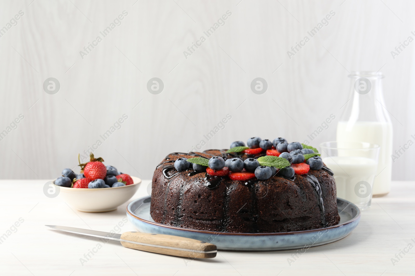 Delicious chocolate bundt cake with strawberries, mint and blueberries on light table Photo of Delicious chocolate bundt cake with strawberries, mint and blueberries on light table