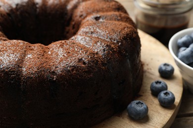 Photo of Delicious chocolate bundt cake with blueberries on wooden table, closeup