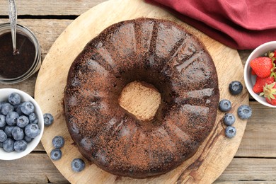 Photo of Delicious chocolate bundt cake, strawberries and blueberries on wooden table, flat lay