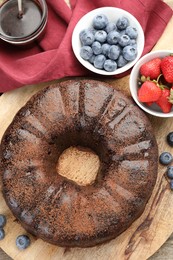 Photo of Delicious chocolate bundt cake, strawberries and blueberries on wooden table, flat lay