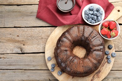 Photo of Delicious chocolate bundt cake, strawberries and blueberries on wooden table, flat lay. Space for text