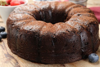 Photo of Delicious chocolate bundt cake with blueberries on wooden table, closeup