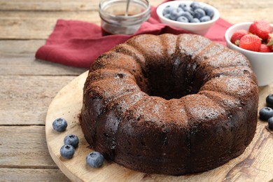 Photo of Delicious chocolate bundt cake with blueberries on wooden table, closeup