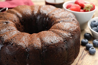 Photo of Delicious chocolate bundt cake with blueberries on wooden table, closeup