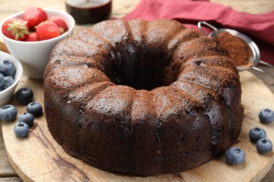 Photo of Delicious chocolate bundt cake with blueberries on wooden table, closeup