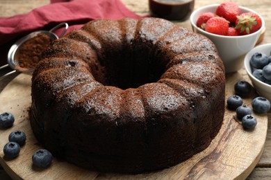 Photo of Delicious chocolate bundt cake with blueberries on wooden table, closeup