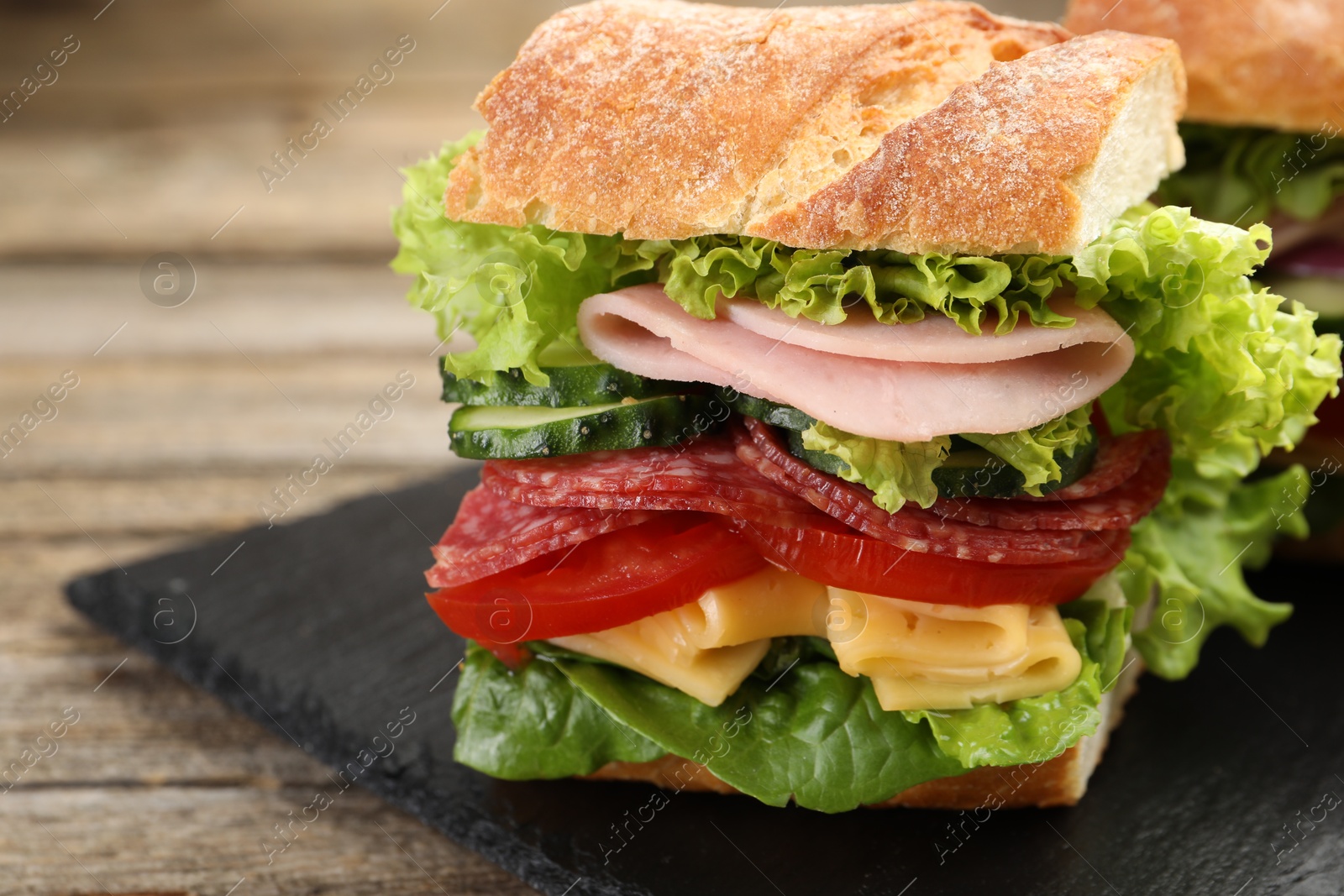 Tasty baguette sandwich with ham and vegetables on wooden table, closeup Photo of Tasty baguette sandwich with ham and vegetables on wooden table, closeup