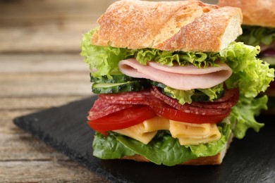 Photo of Tasty baguette sandwich with ham and vegetables on wooden table, closeup