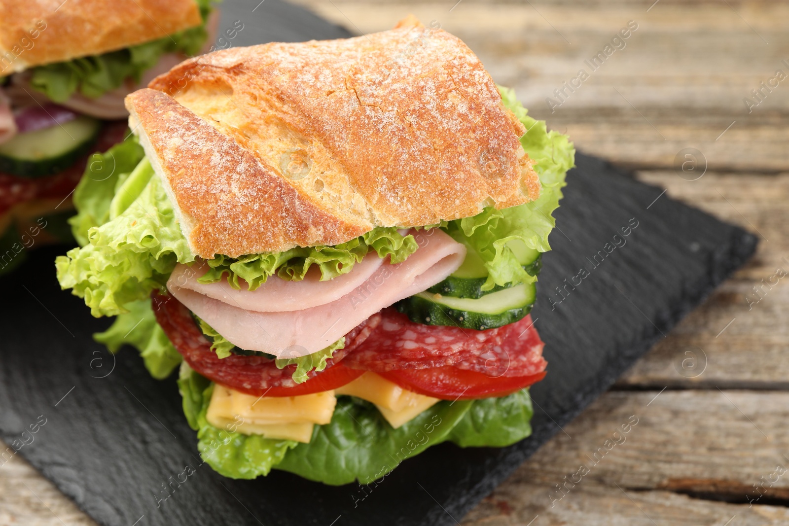 Tasty baguette sandwich with ham and vegetables on wooden table, closeup Photo of Tasty baguette sandwich with ham and vegetables on wooden table, closeup