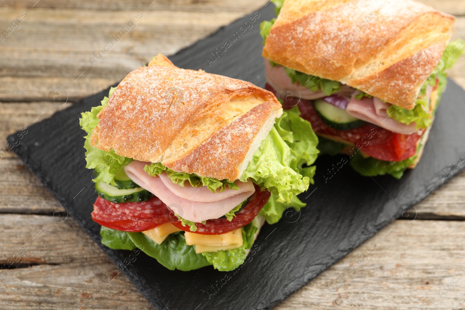 Tasty baguette sandwich with ham and vegetables on wooden table, closeup Photo of Tasty baguette sandwich with ham and vegetables on wooden table, closeup
