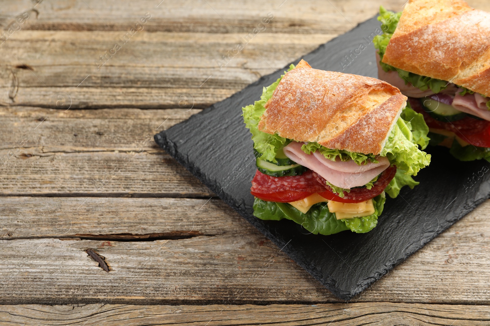 Tasty baguette sandwich with ham and vegetables on wooden table, closeup. Space for text Photo of Tasty baguette sandwich with ham and vegetables on wooden table, closeup. Space for text
