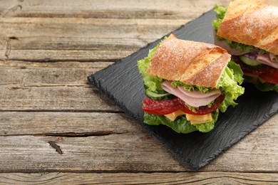 Photo of Tasty baguette sandwich with ham and vegetables on wooden table, closeup. Space for text