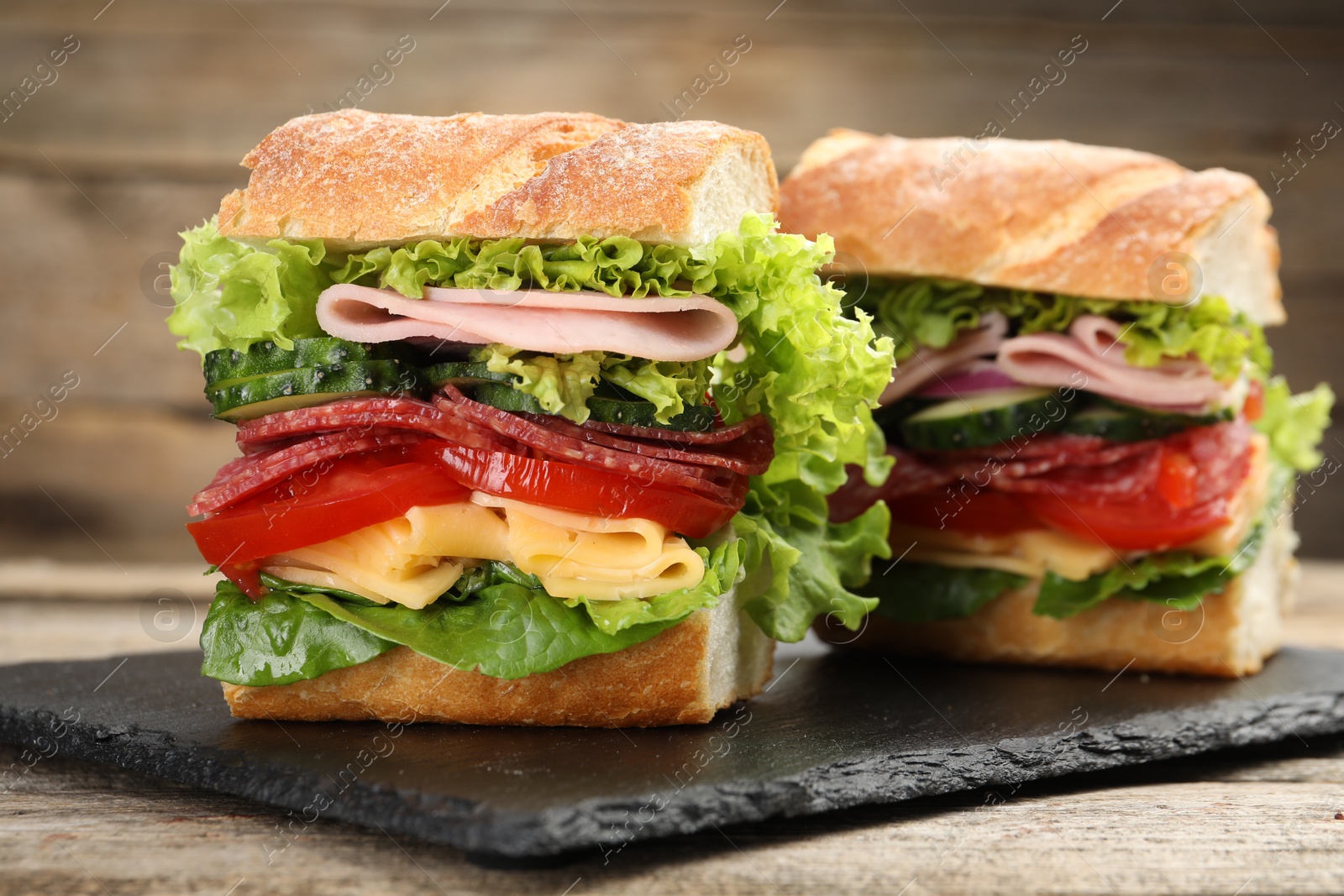 Tasty baguette sandwich with ham and vegetables on wooden table, closeup Photo of Tasty baguette sandwich with ham and vegetables on wooden table, closeup