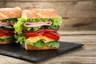 Photo of Tasty baguette sandwich with ham and vegetables on wooden table, closeup. Space for text