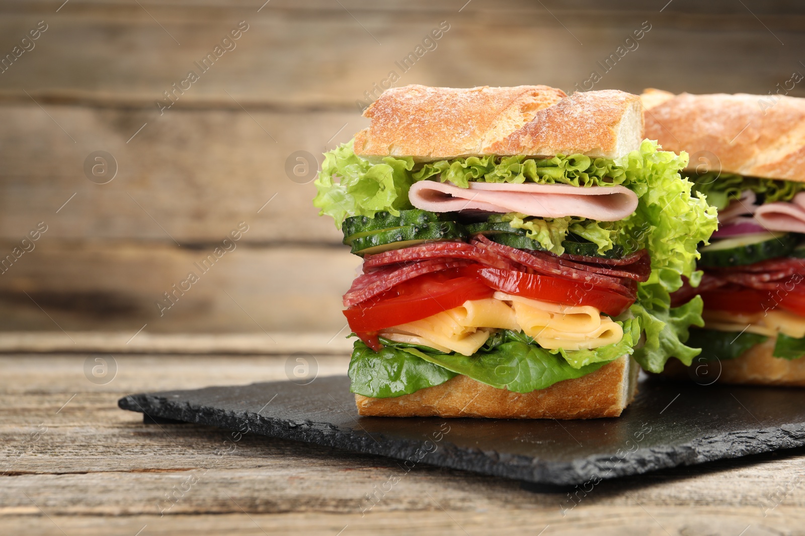 Tasty baguette sandwich with ham and vegetables on wooden table, closeup. Space for text Photo of Tasty baguette sandwich with ham and vegetables on wooden table, closeup. Space for text