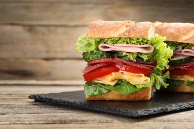 Photo of Tasty baguette sandwich with ham and vegetables on wooden table, closeup. Space for text
